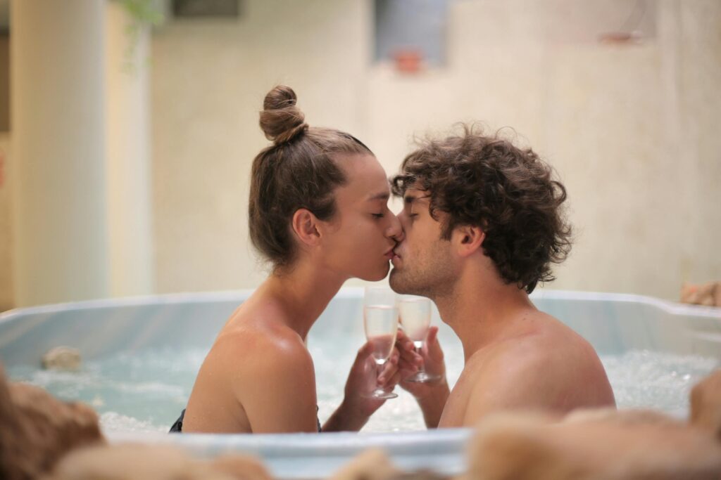 A couple sharing a kiss in a hot tub, celebrating with glasses of champagne, creating a romantic atmosphere.