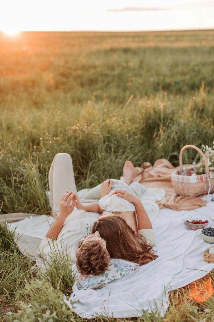 Couple enjoying a serene sunset picnic in a lush green field with a cozy blanket.