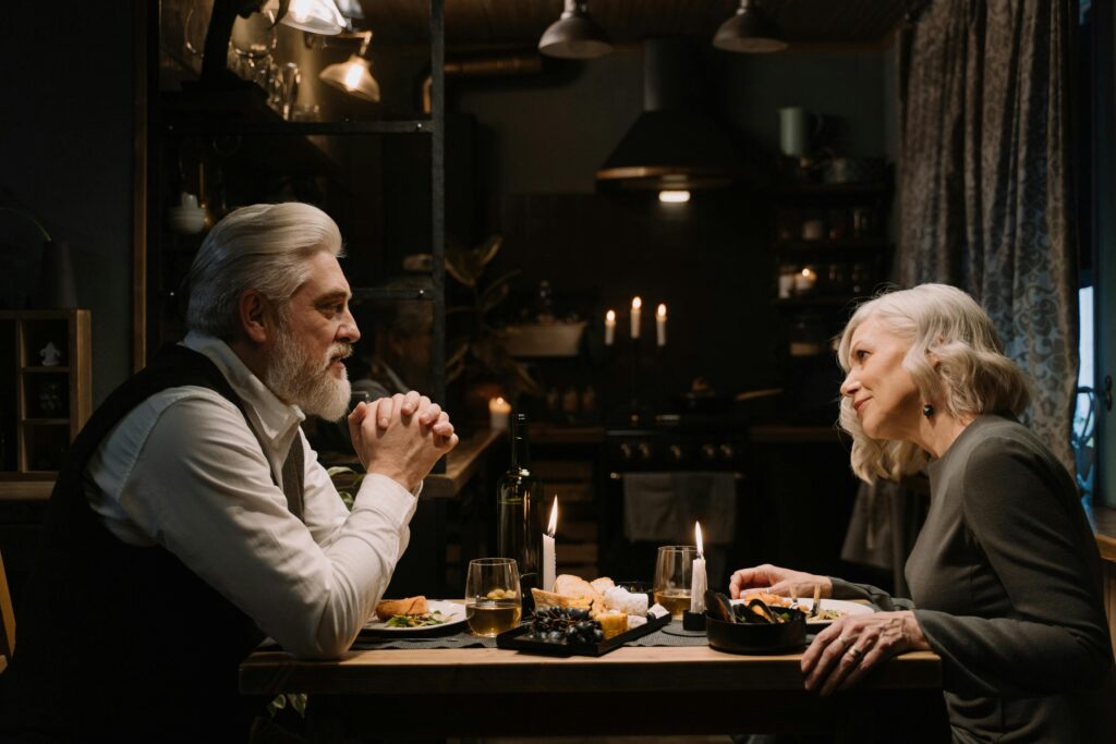 A senior couple shares a romantic dinner by candlelight in a cozy home setting, expressing love and companionship.